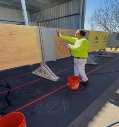 Worker spraying a surface with a paint sprayer on a construction site, wearing safety gear