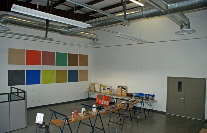 Studio with colorful wall panels, tables displaying materials, and exposed ducts on the ceiling.